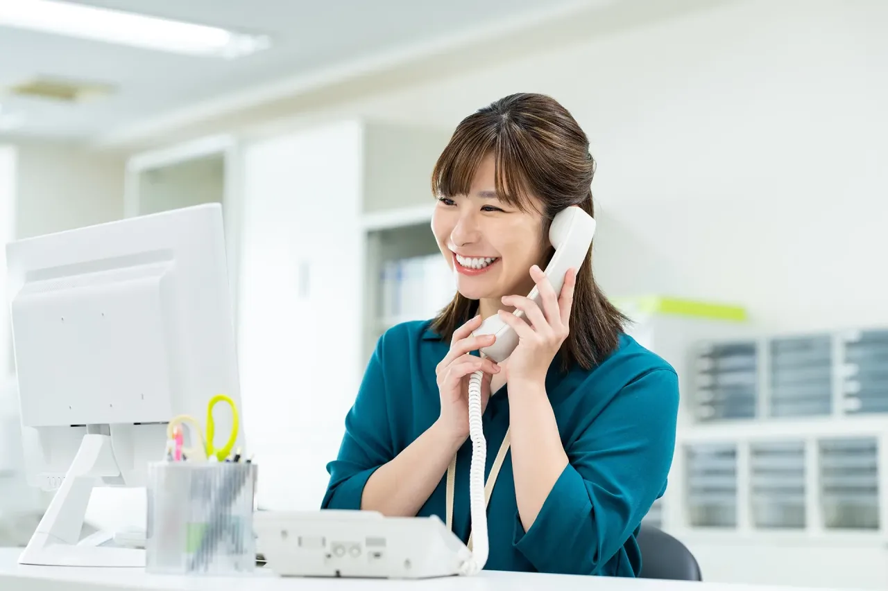 オフィスでPCを前に笑顔で電話対応をする女性社員